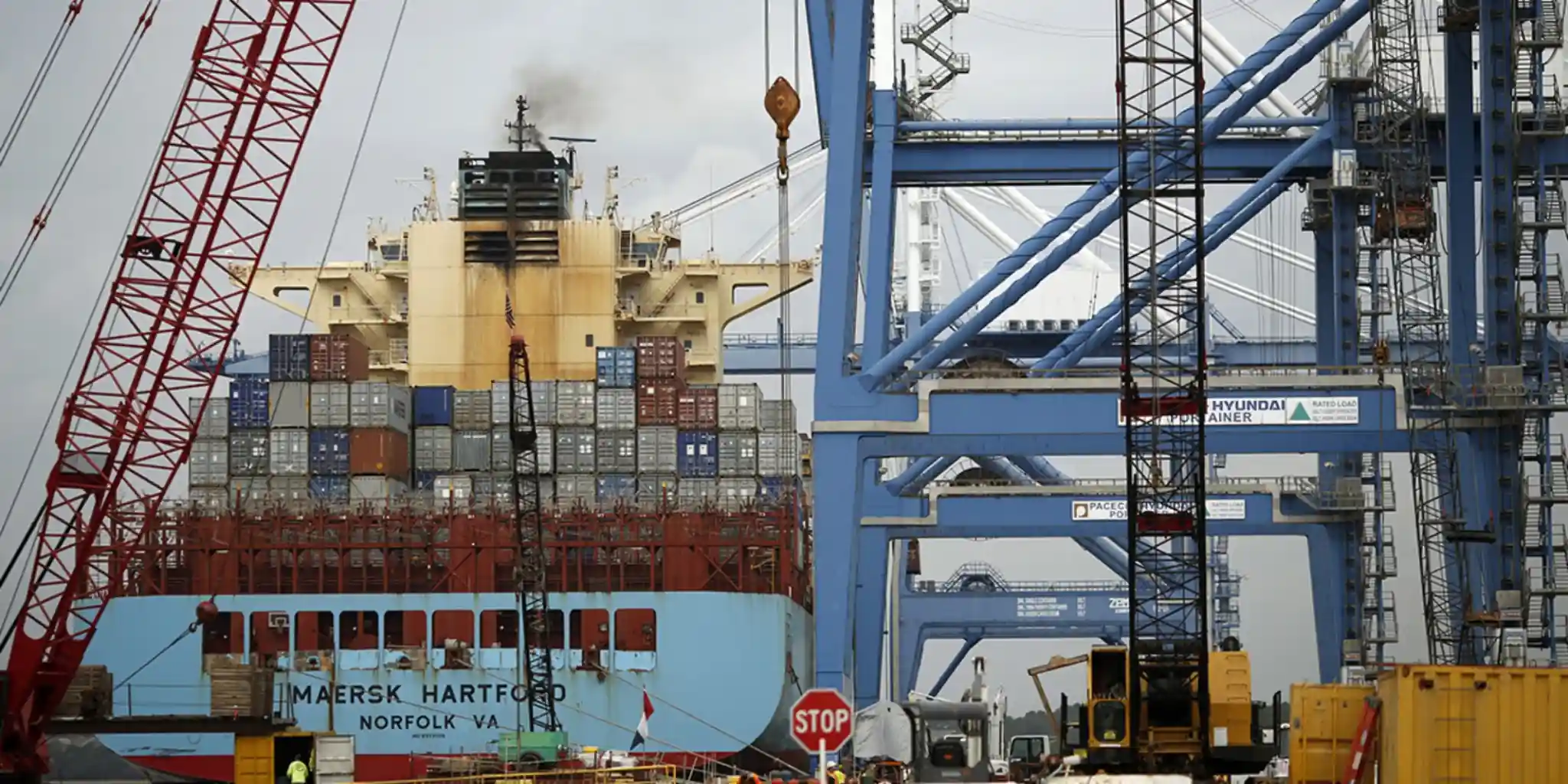 Cargo ship loaded with shipping containers docked beneath large industrial port cranes.