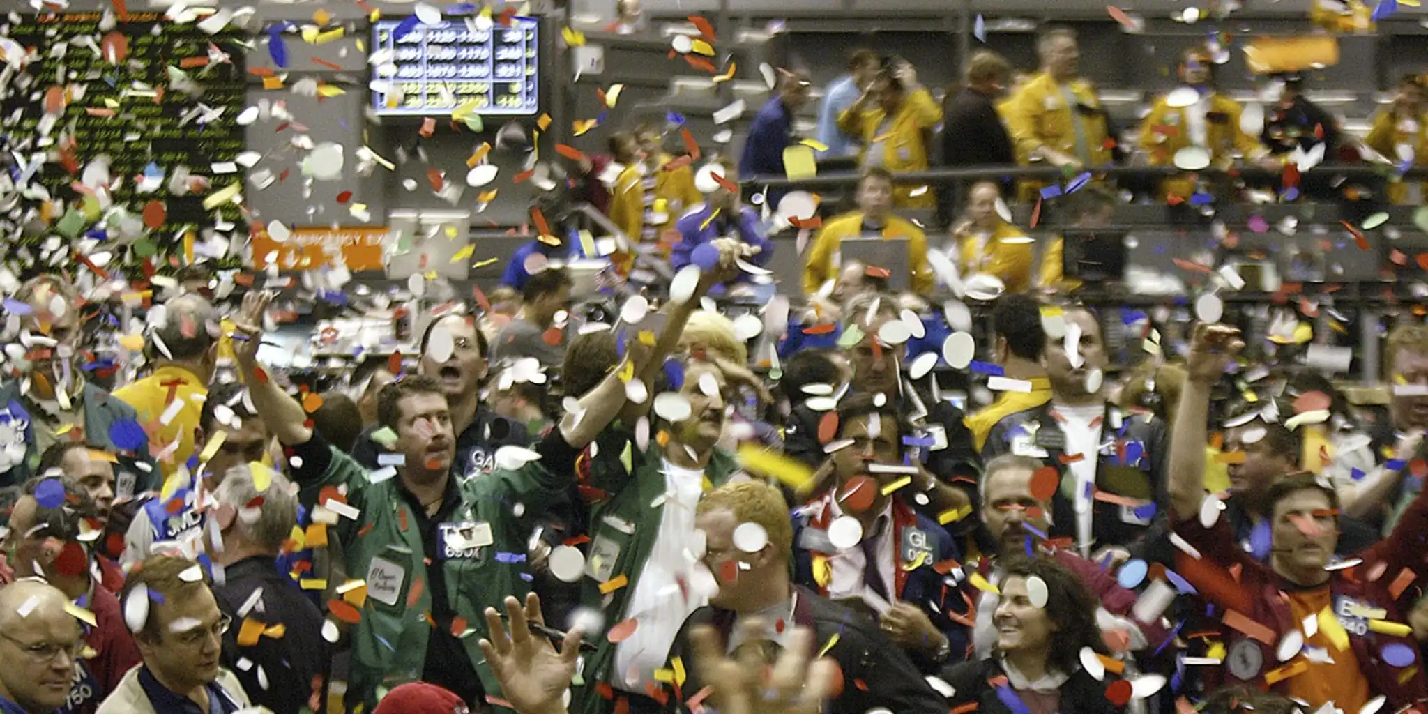 Crowded trading floor with people celebrating as colorful confetti fills the air.