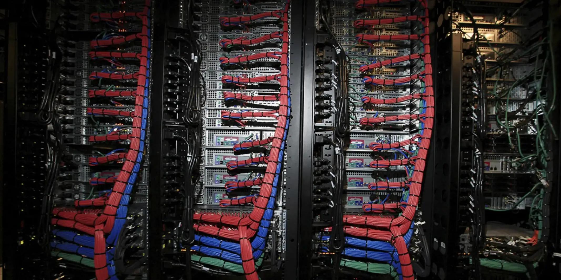 Server racks filled with computer hardware and neatly bundled red, blue, and green network cables.