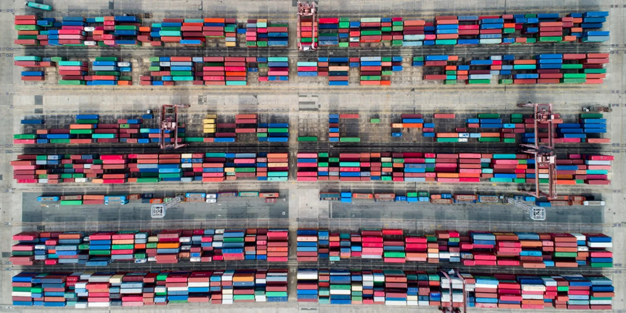 Aerial view of a shipping container terminal with rows of colorful cargo containers and loading cranes.