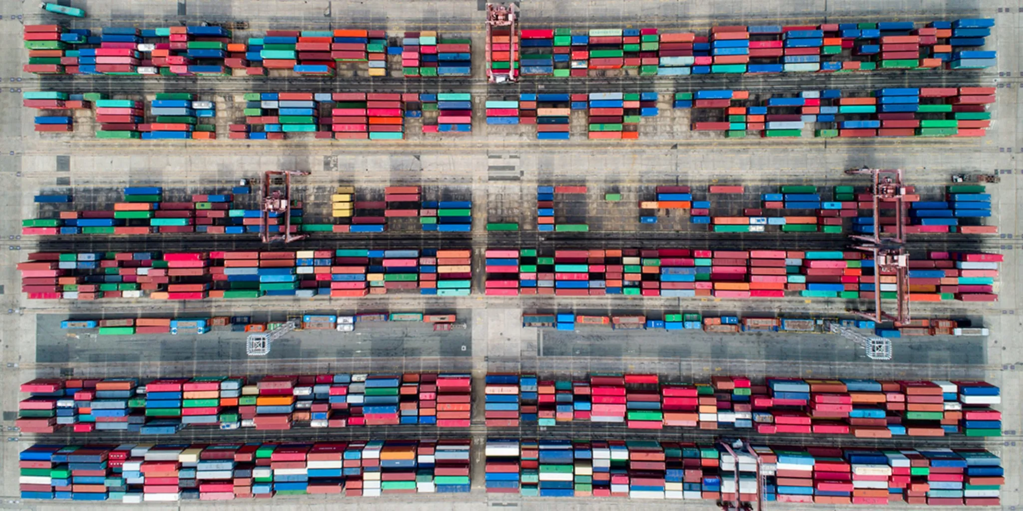 Aerial view of a shipping container terminal with rows of colorful cargo containers and loading cranes.