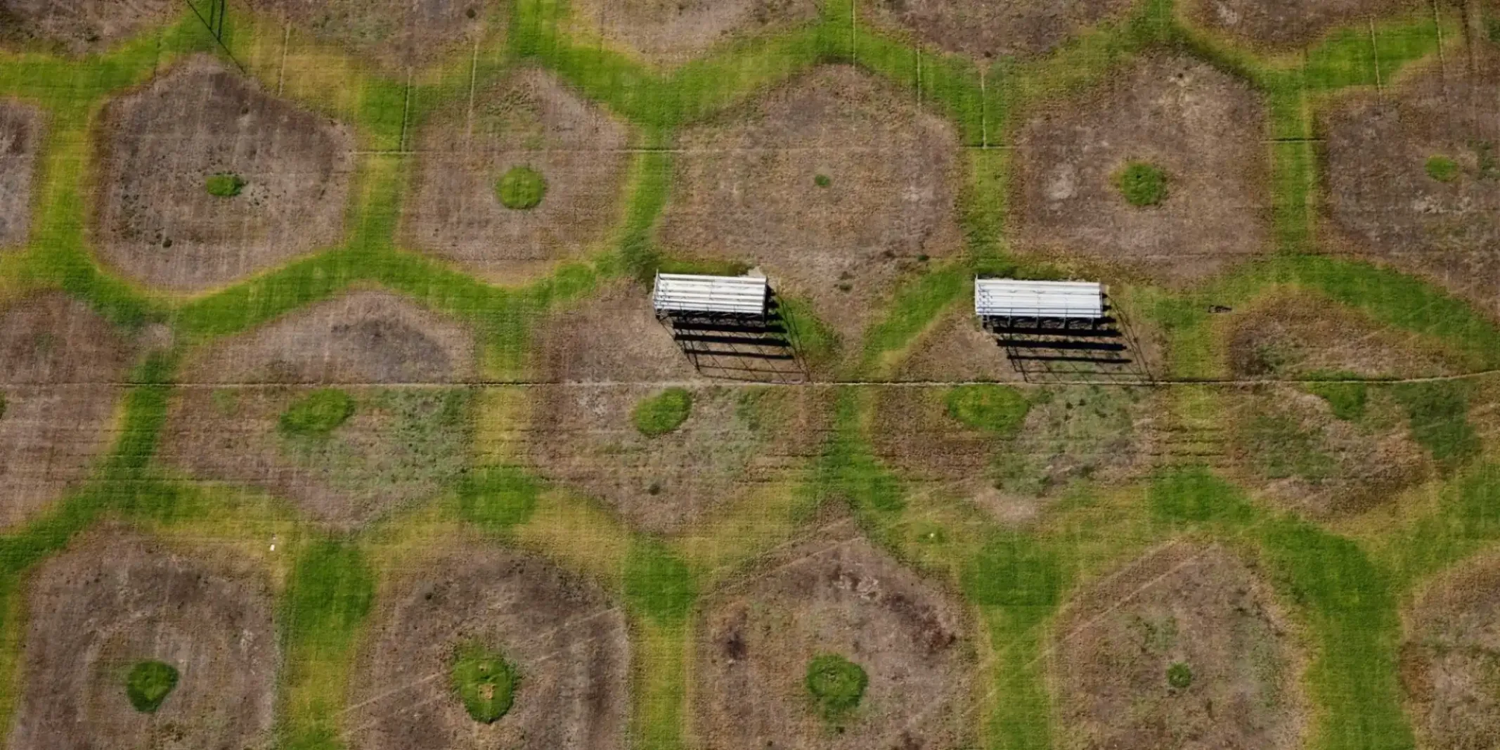 Aerial view of a patterned grassy field with winding green paths and two white bleachers.