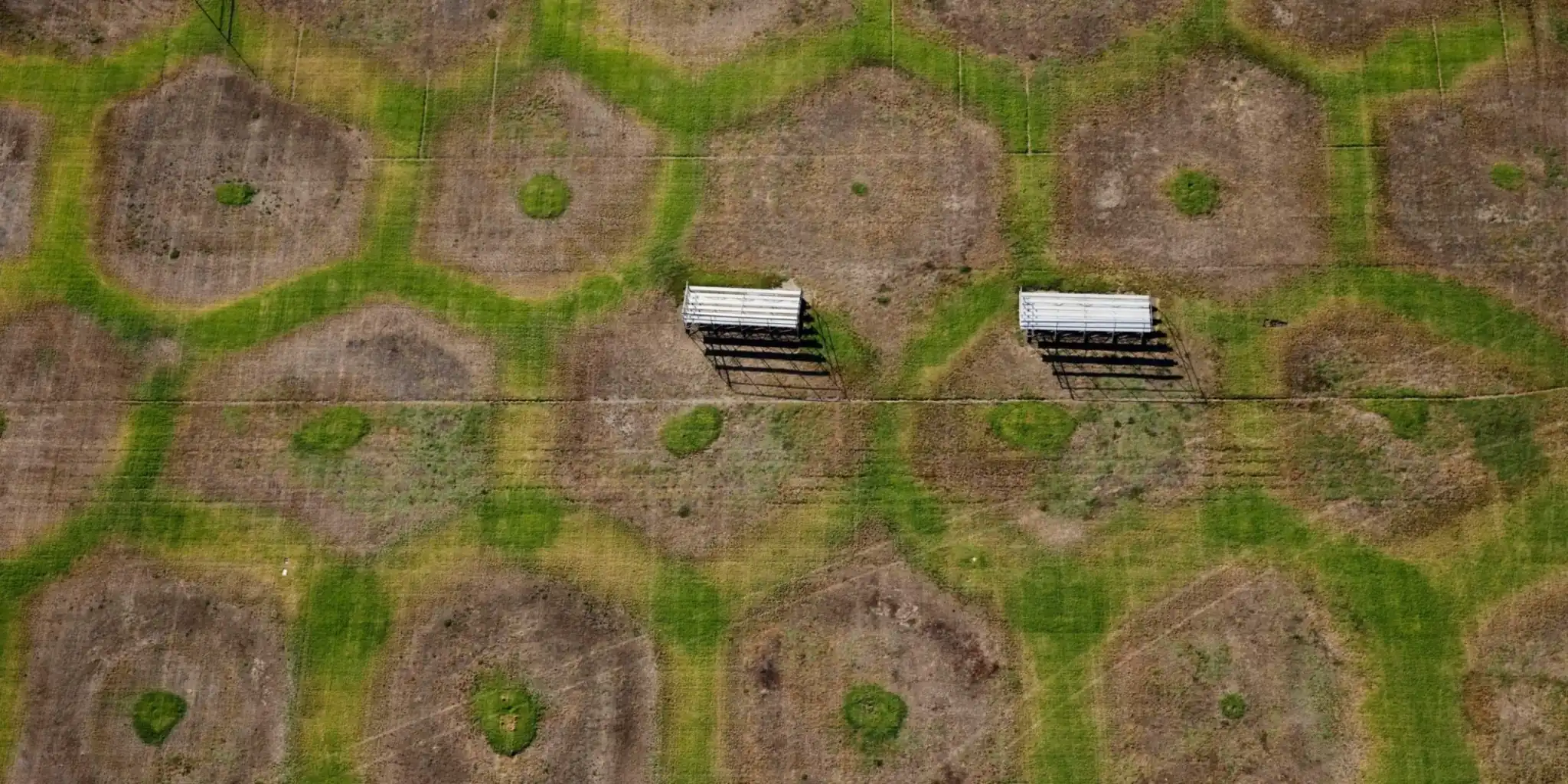 Aerial view of a patterned grassy field with winding green paths and two white bleachers.