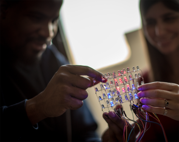 Two people working on making electric connections to light up a small grid of light bulbs