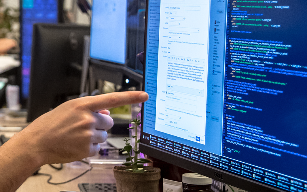 Cropped image of a finger pointing at a desktop computer screen with text and data on it