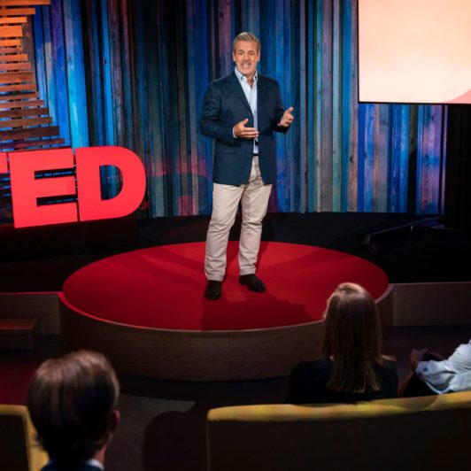 Warren Valdmanis on the TED Talk stage, speaking animatedly