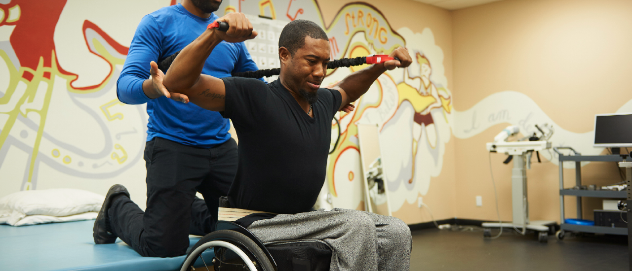Man in a wheelchair exercises with a personal trainer.