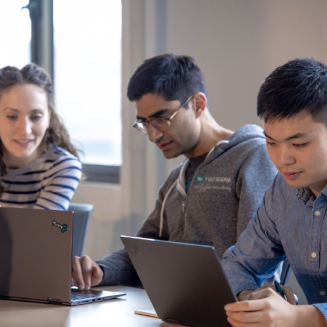 Diverse group of grad students work on laptops in an office.