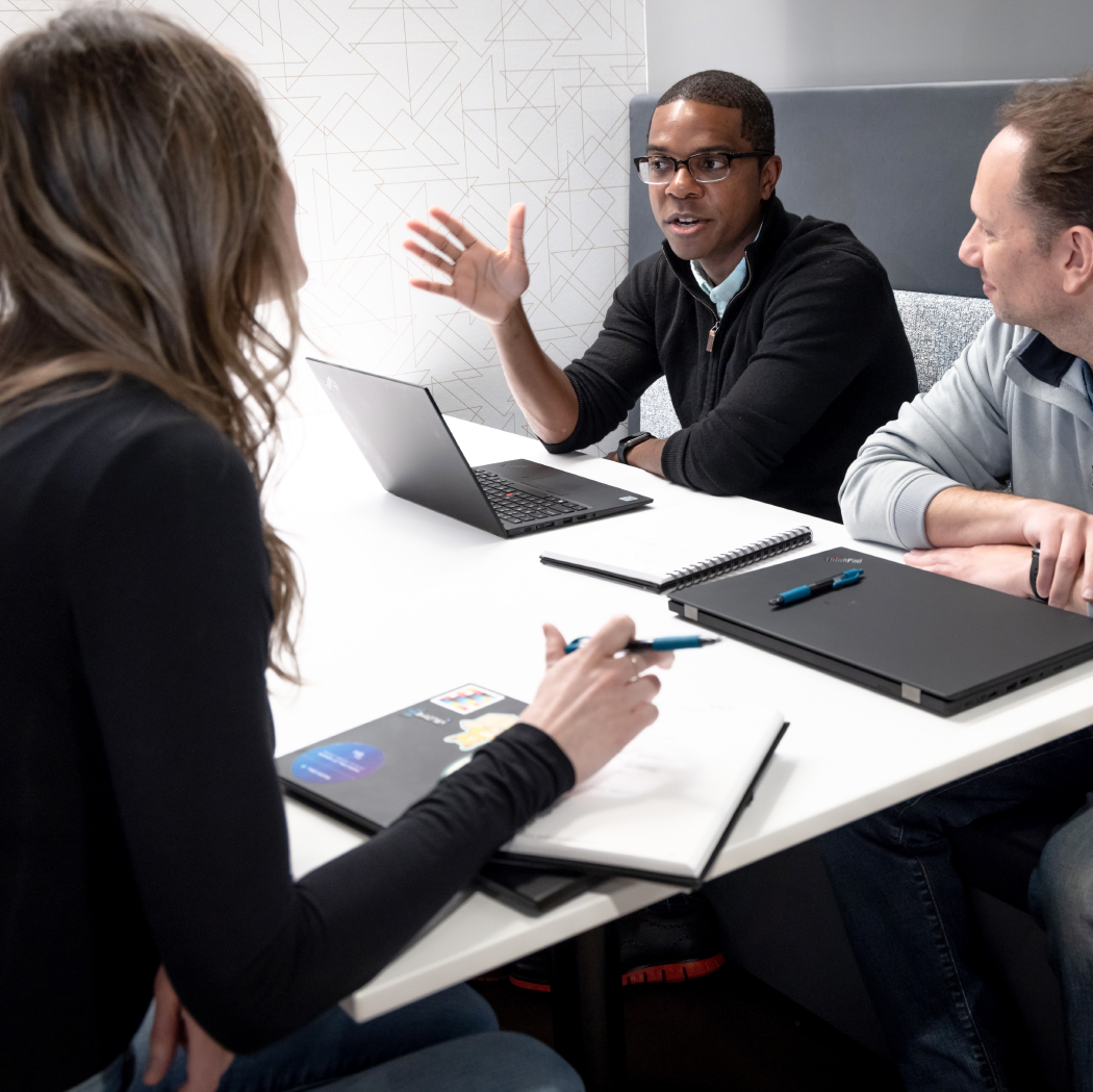 Three faculty members sit at a table having a discussion.