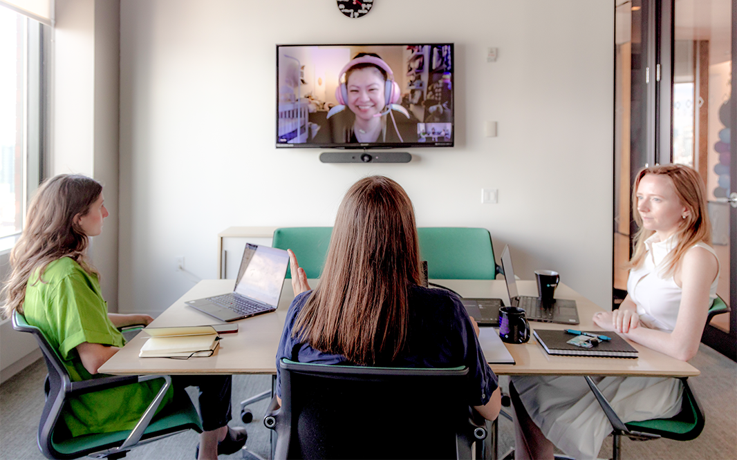 Employees sit in a conference room conducting a video chat with another employee who is working from home.