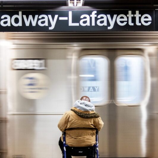 Man with a walker waits on a New York City subway platform.