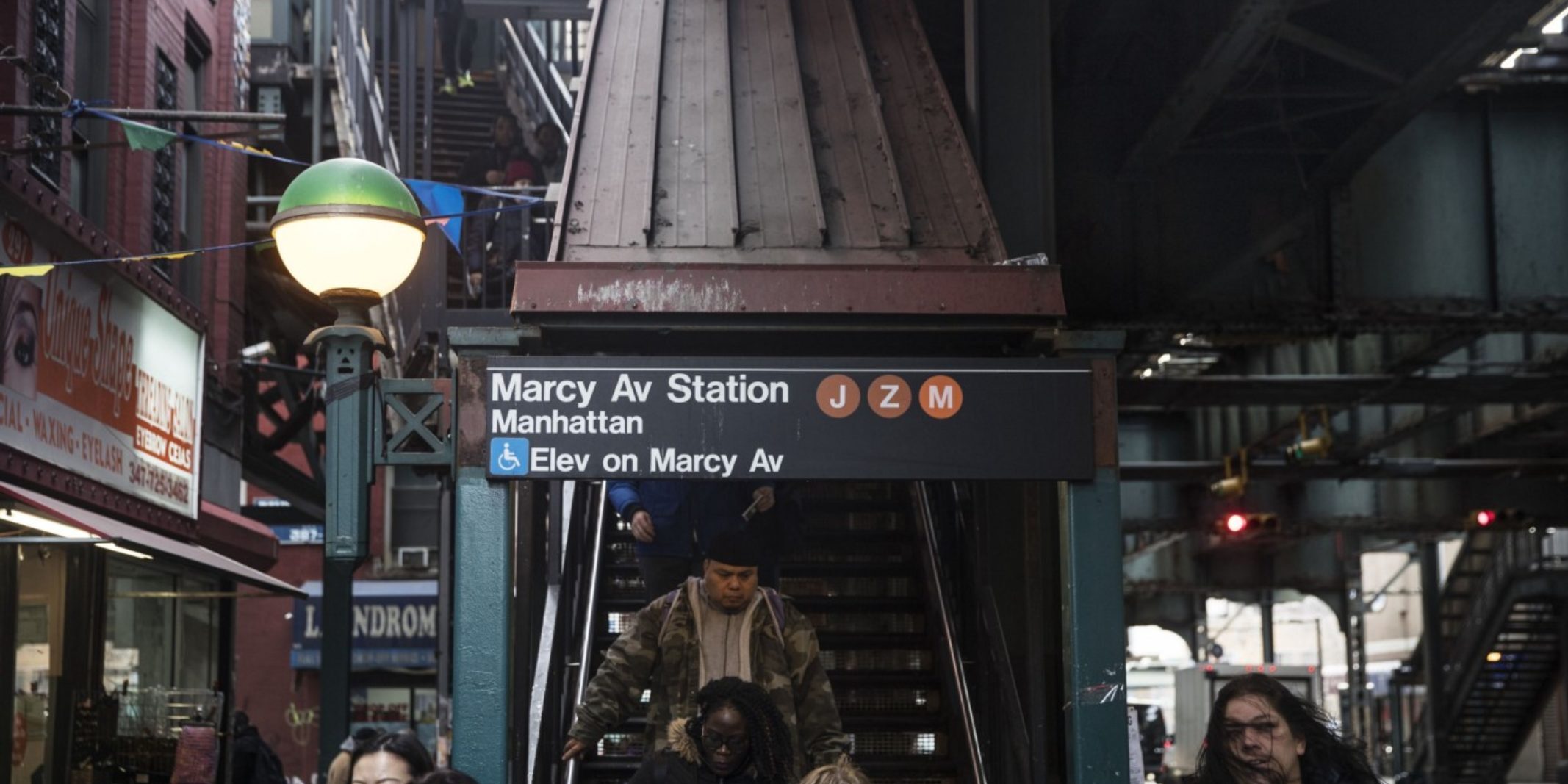 Outdoor stairwell leading to the NYC subway with a sign displaying that there is also an elevator available on the avenue.