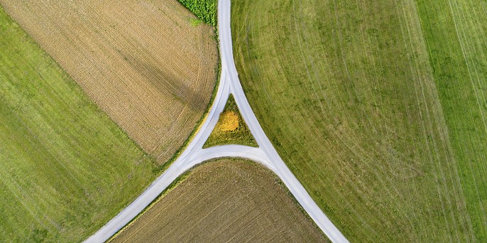 Aerial view of farmland fields in green and brown patches converging around a Y-shaped road intersection.