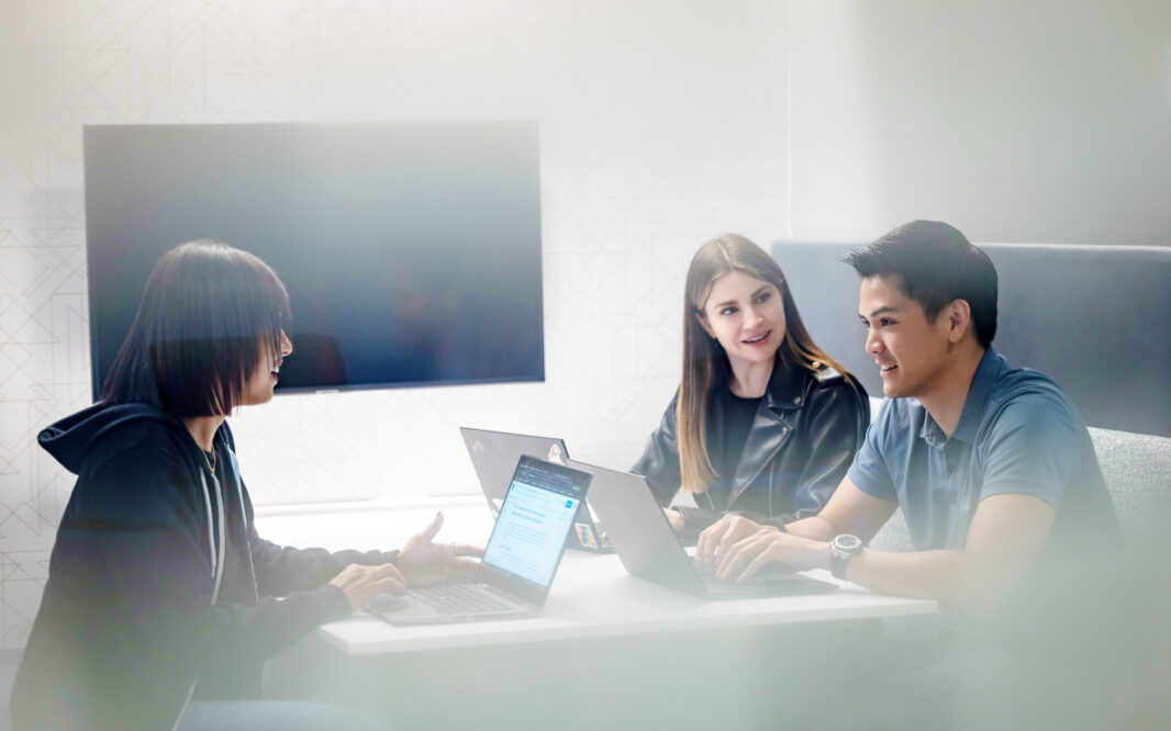 Three Two Sigma engineers collaborate at a table with their laptops.