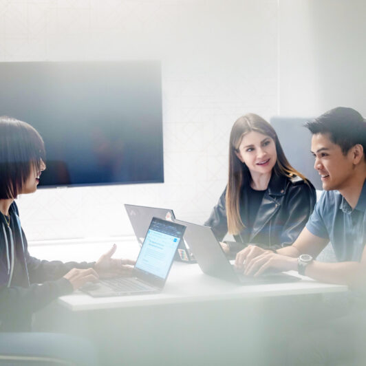 Three Two Sigma engineers collaborate at a table with their laptops.