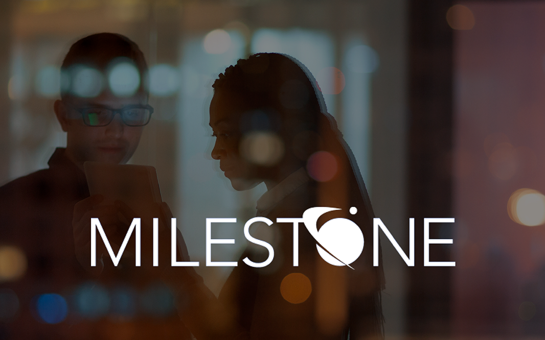 Milestone logo with two employees in an office looking at a tablet.