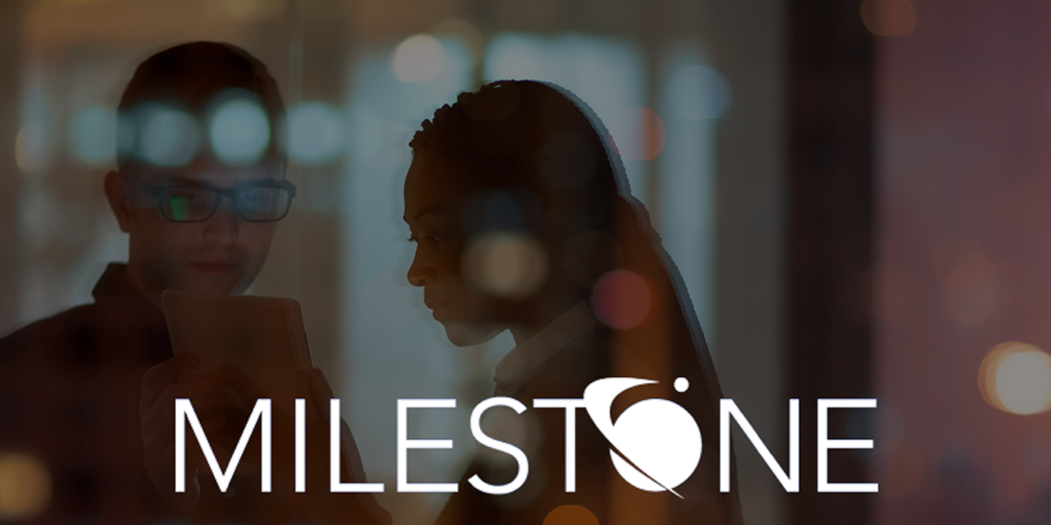 Milestone logo with two employees in an office looking at a tablet.
