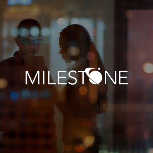 Milestone logo with two employees in an office looking at a tablet.