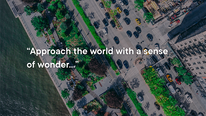 Aerial view of a tree-lined city street beside a river, overlaid with the quote 'Approach the world with a sense of wonder...'