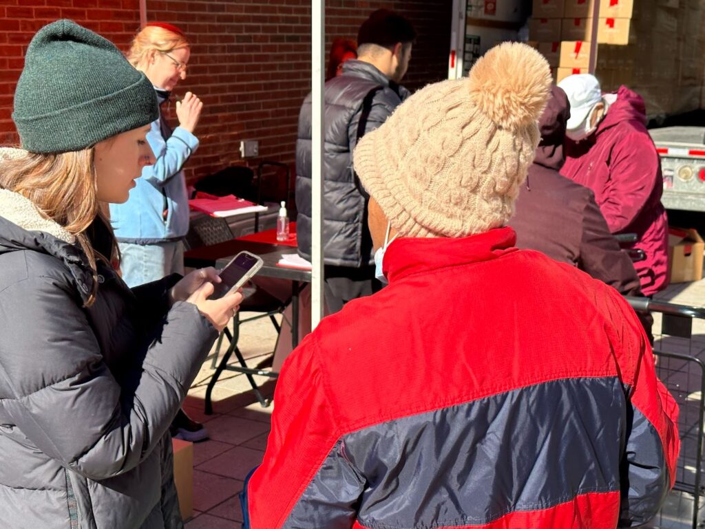 A Wellfare volunteer looks at her phone on the left, and a Wellfare costumer stands with their back to the camera on the right