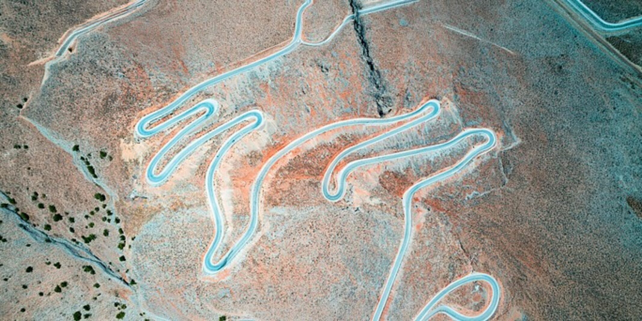 Aerial view of winding desert switchback roads in orange and teal tones resembling a tangled loop pattern.