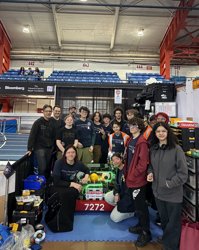 A student robotics team poses with their competition robot at an indoor arena event featuring Two Sigma and Bloomberg sponsor banners.