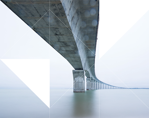 Low-angle view of a long concrete bridge extending over calm water, framed by geometric triangular graphic overlays.