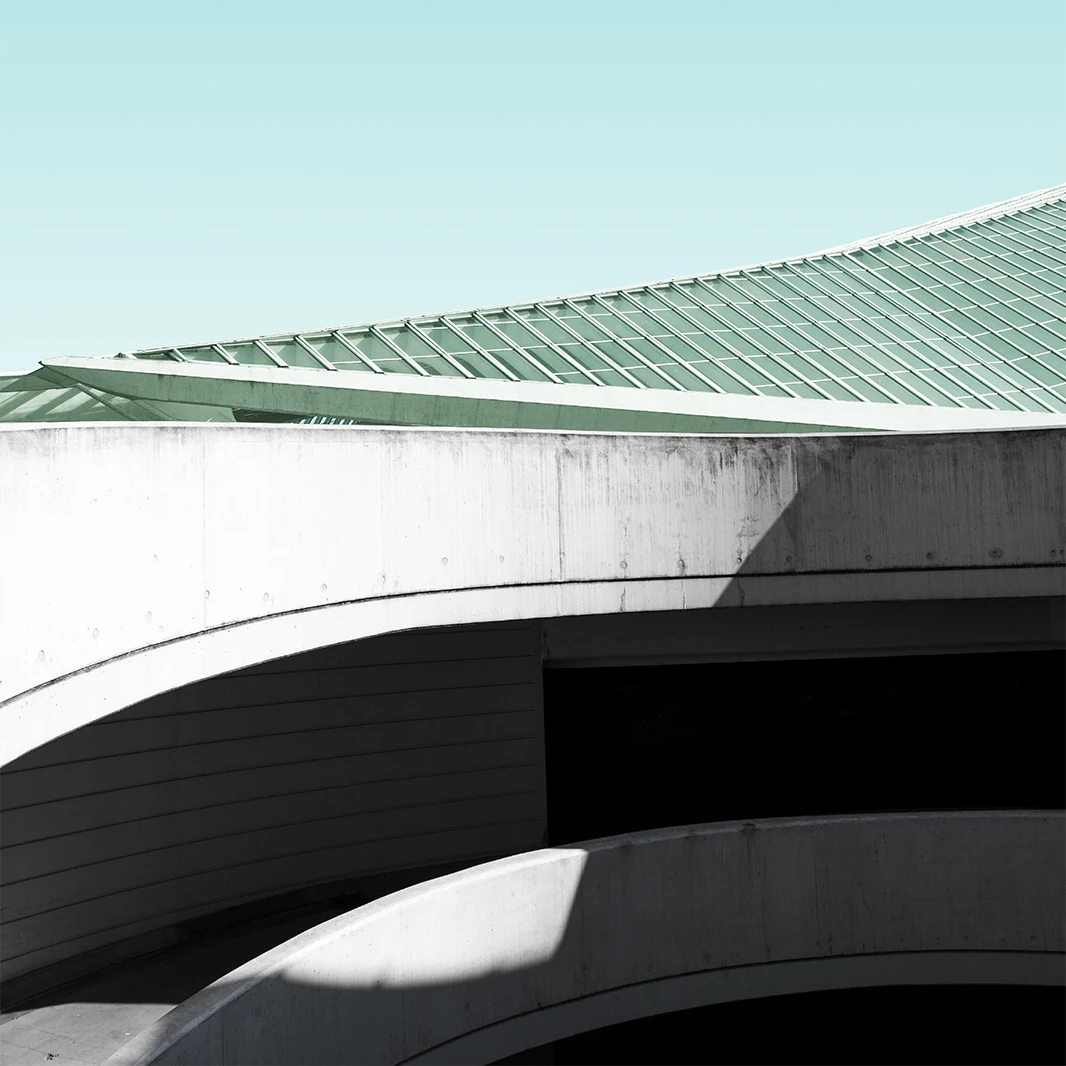 Modern architectural roof with green-tinted glass panels above a curved concrete structure under a pale blue sky.