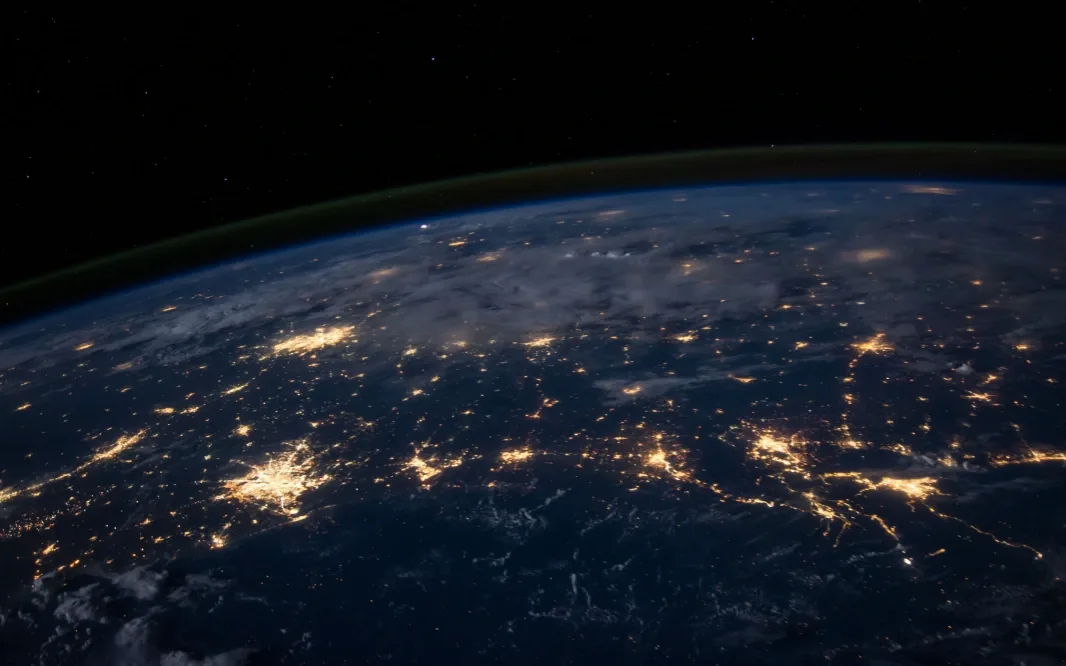 View of Earth at night from space with illuminated cities and cloud cover.