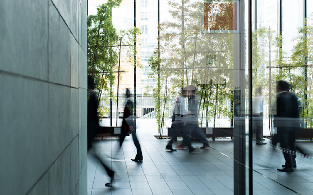 People walking through a modern glass building interior with trees visible outside and motion blur capturing movement