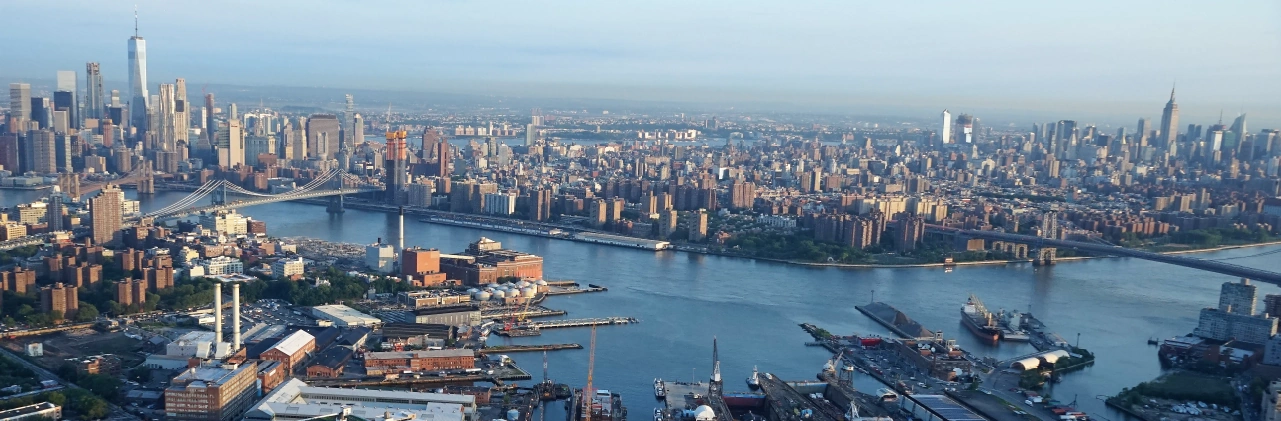 Aerial view of New York City waterfront, with bridges spanning the East River and the Manhattan skyline in the distance.