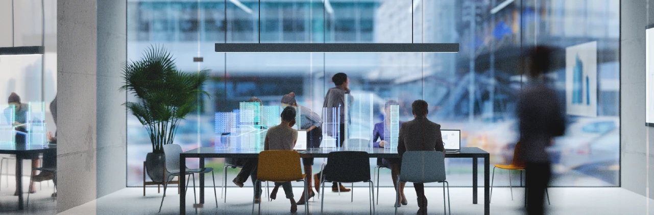 People meeting in a modern glass-walled office with translucent digital building graphics above the table.