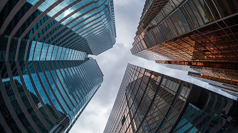 Upward view of glass skyscrapers converging toward a cloudy sky, shot from street level.
