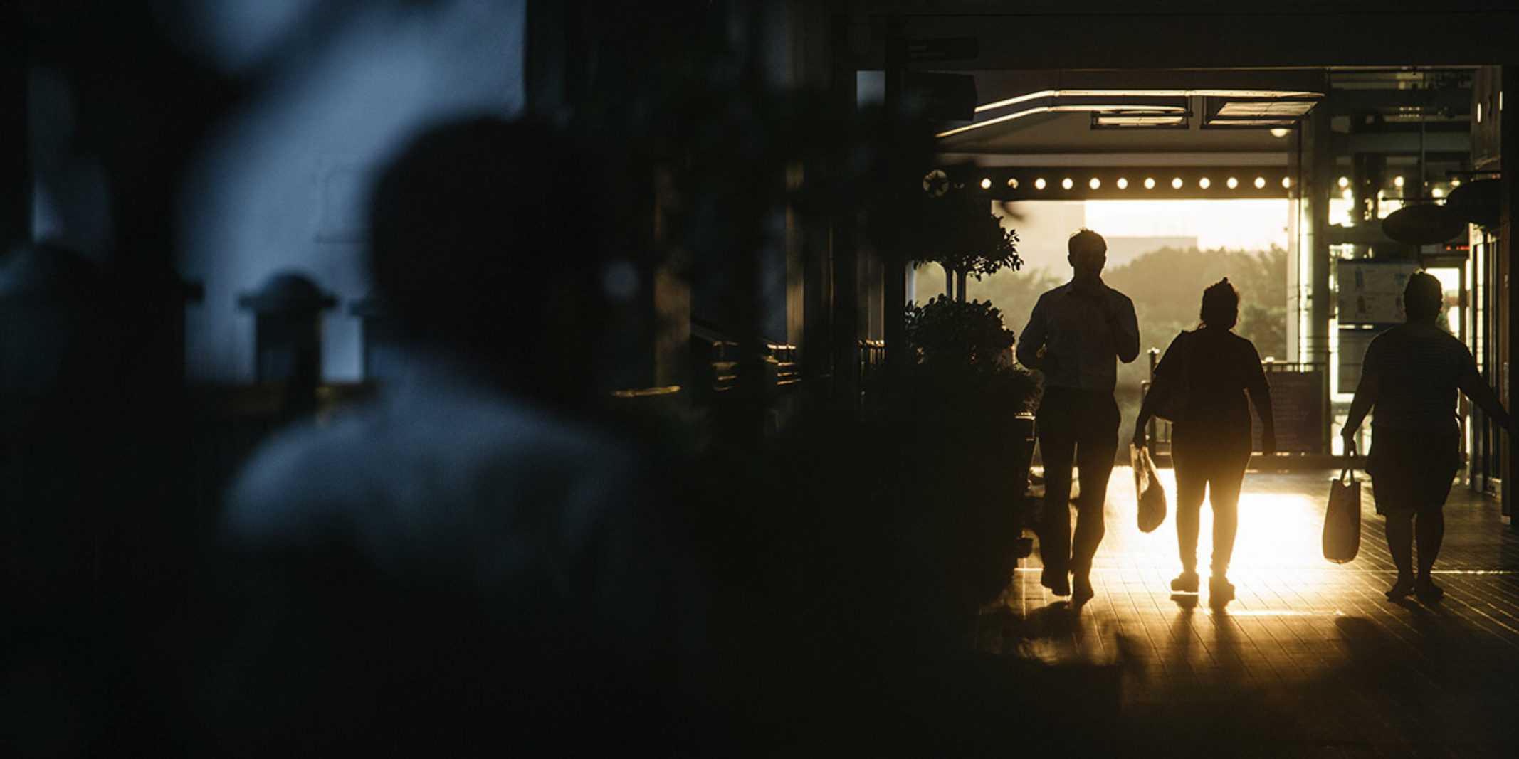 3 people walking down a hall way that is dark because of the sunset