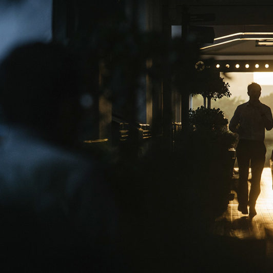 3 people walking down a hall way that is dark because of the sunset