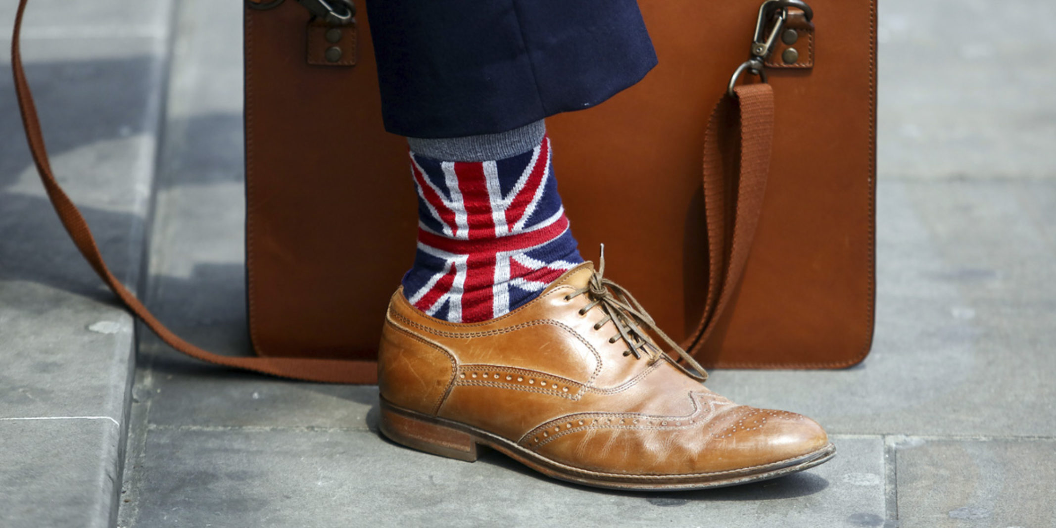 guy sitting down in a suit wearing UK flag sock with his brief case by his foot