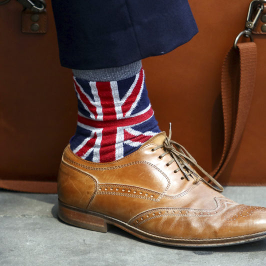 guy sitting down in a suit wearing UK flag sock with his brief case by his foot