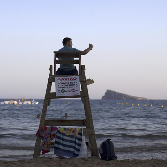 Picture of a lifeguard while he sits on his chair looking into the water