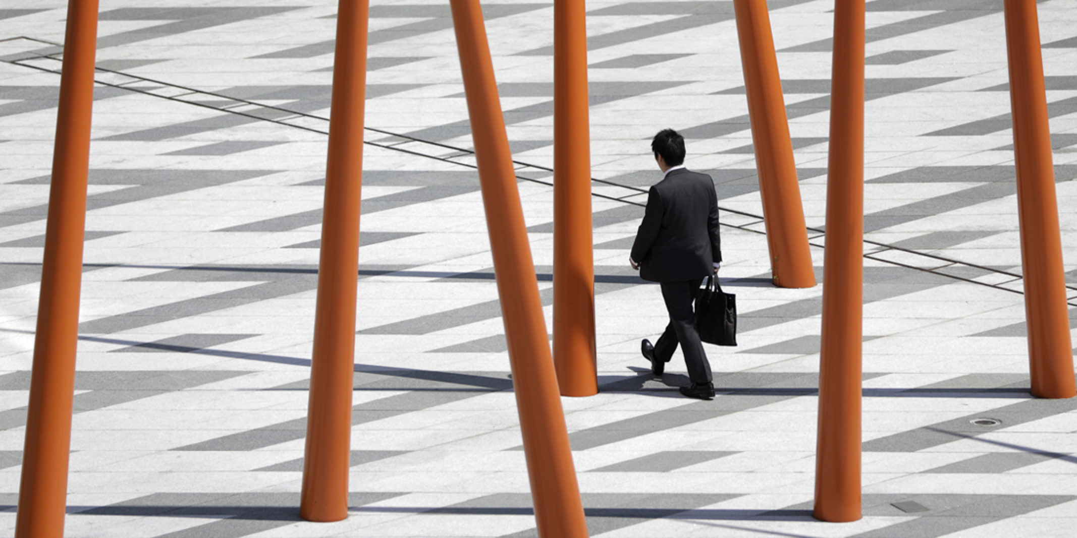 Man in suit walking through a street with a bunch of red pillars around him