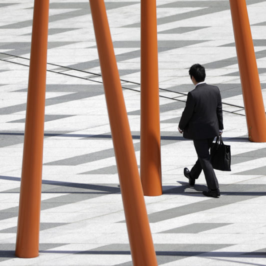 Man in suit walking through a street with a bunch of red pillars around him